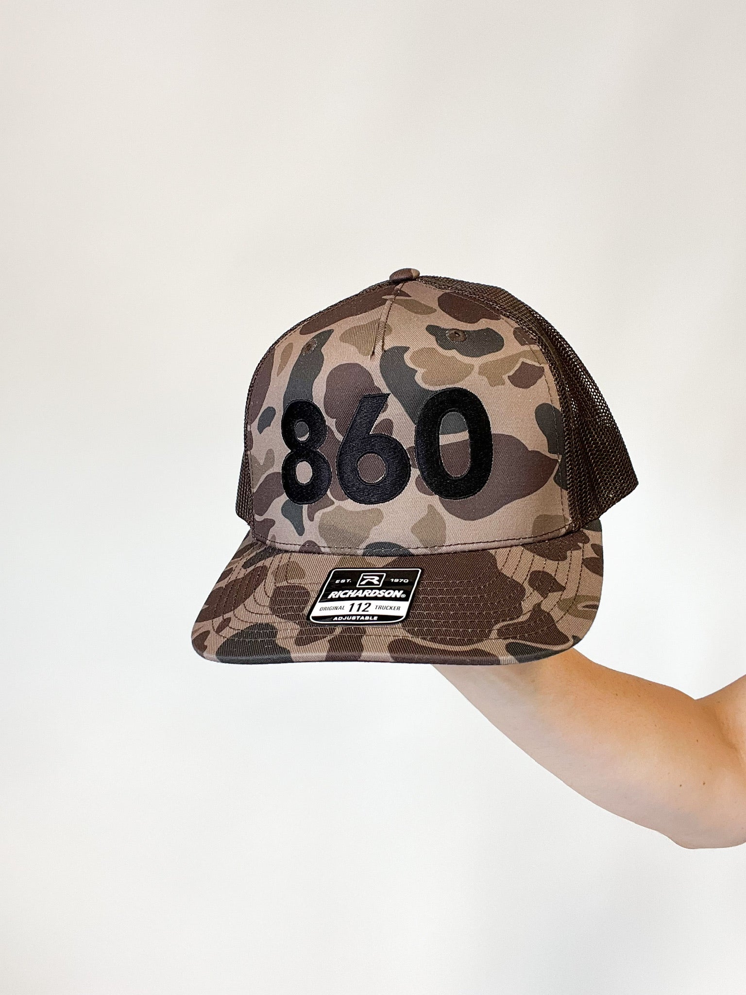 camo trucker hat with black 860 embroidered on the front, black Anchored American embroidered on the back
