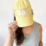 yellow baseball hat, white 860 embroidered on the front, white Anchored American embroidered on the back, leather strap adjuster