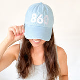 Light blue baseball cap, white 860 embroidered on the front of the hat, white Anchored American embroidered on the back, leather adjuster strap