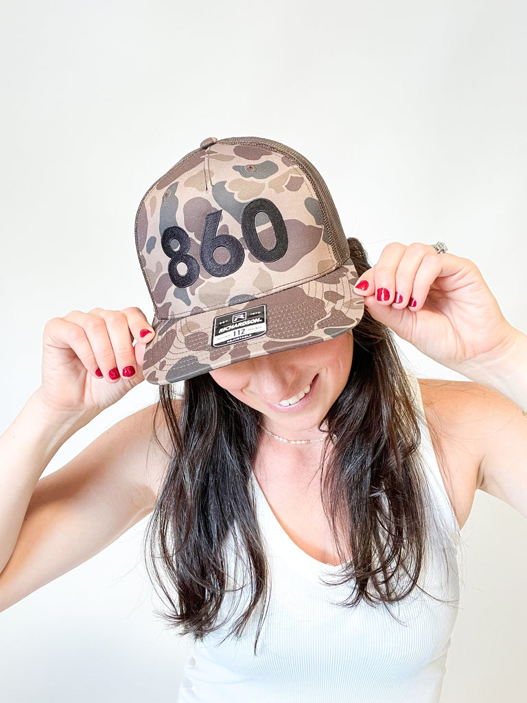 camo trucker hat with black 860 embroidered on the front, black Anchored American embroidered on the back