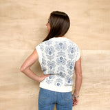White sweater vest with blue floral detail, white pocket on right side, white detail on the collar and bottom, relax fit