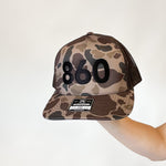 camo trucker hat with black 860 embroidered on the front, black Anchored American embroidered on the back