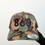 camo trucker hat with black 860 embroidered on the front, black Anchored American embroidered on the back