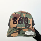 camo trucker hat with black 860 embroidered on the front, black Anchored American embroidered on the back