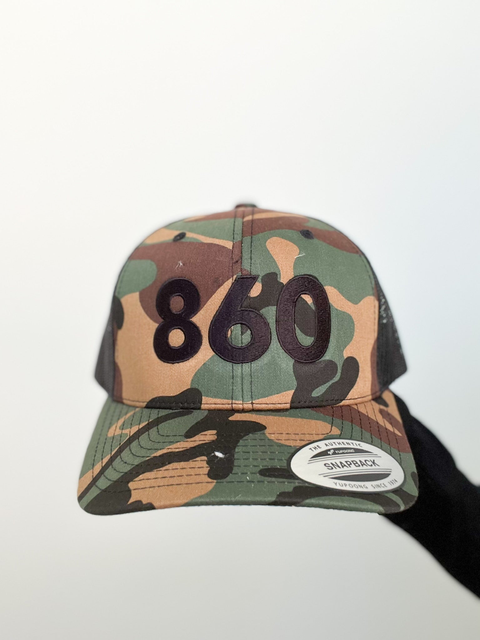 camo trucker hat with black 860 embroidered on the front, black Anchored American embroidered on the back